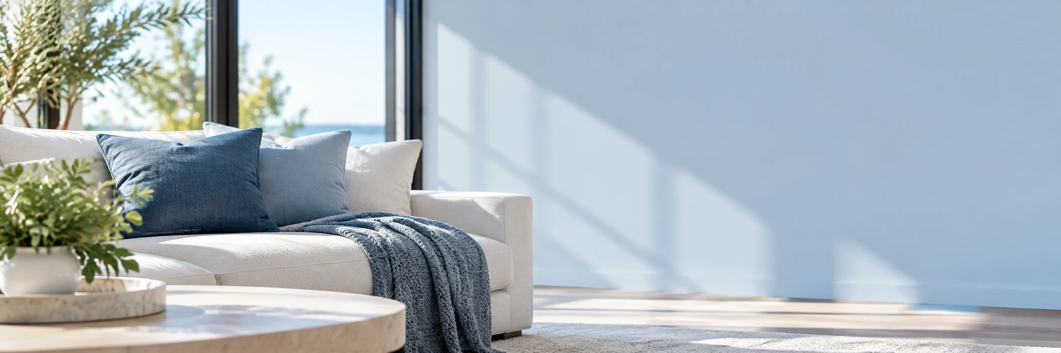 A bright coastal living room with navy and powder-blue pillows beside an open blue wall